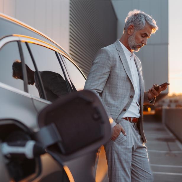Man posing staring at a mobile phone beside a car